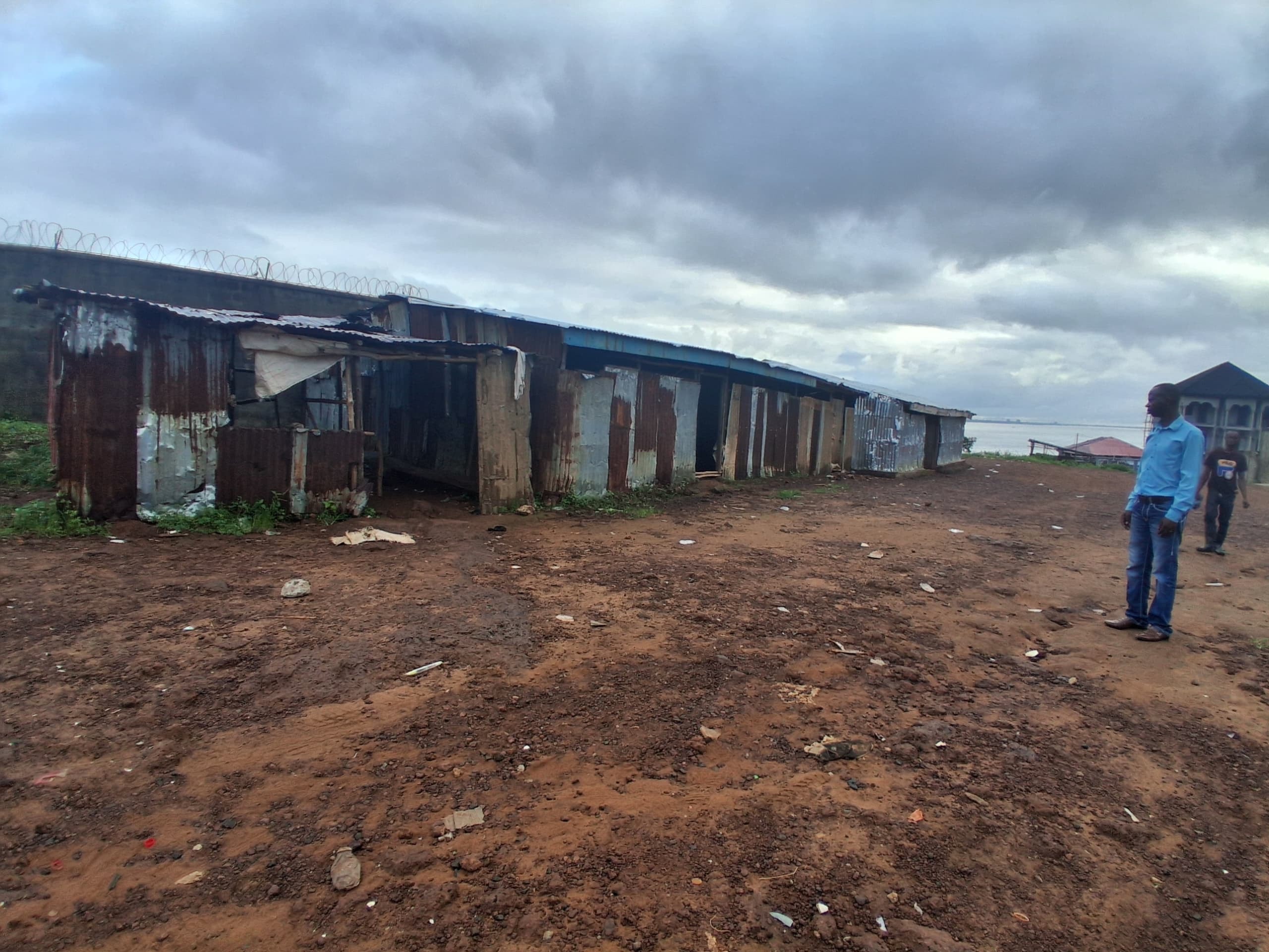 Exterior view of the school building — zinc sheet structure in Sierra Leone with a man surveying the grounds