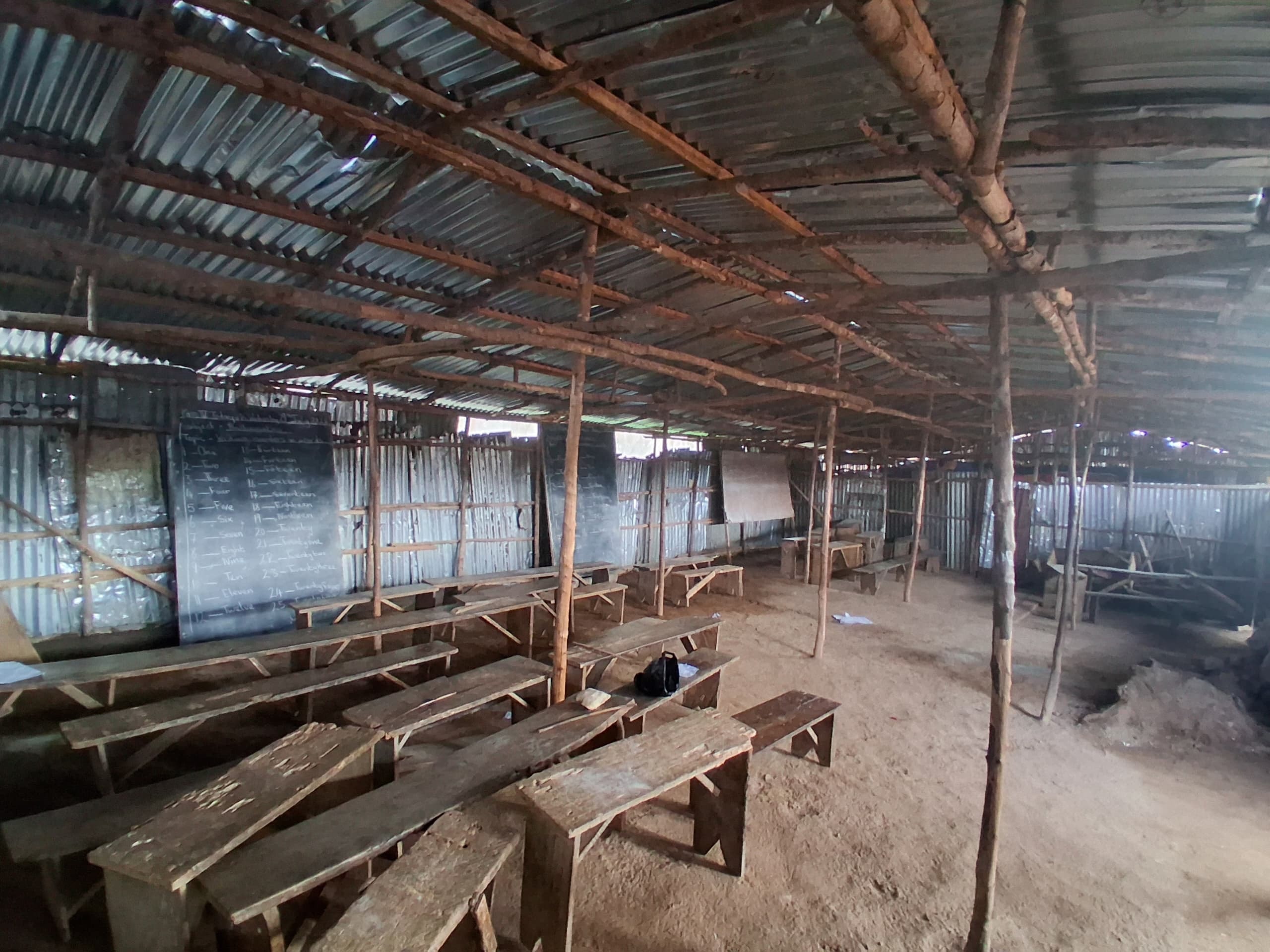 Classroom interior showing rows of wooden benches and chalkboard lessons written on the walls